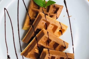 Un plato de waffles con almíbar de chocolate y una hoja de menta como adorno.