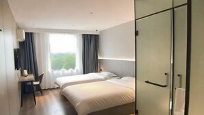 Ein Hotelzimmer mit zwei Betten, einem Schreibtisch und einem großen Fenster mit Vorhängen.
