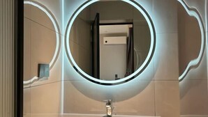 A modern bathroom with a circular mirror, a sink, and a shower area. - Jingdezhen International Youth Hostel (Jingdezhen)