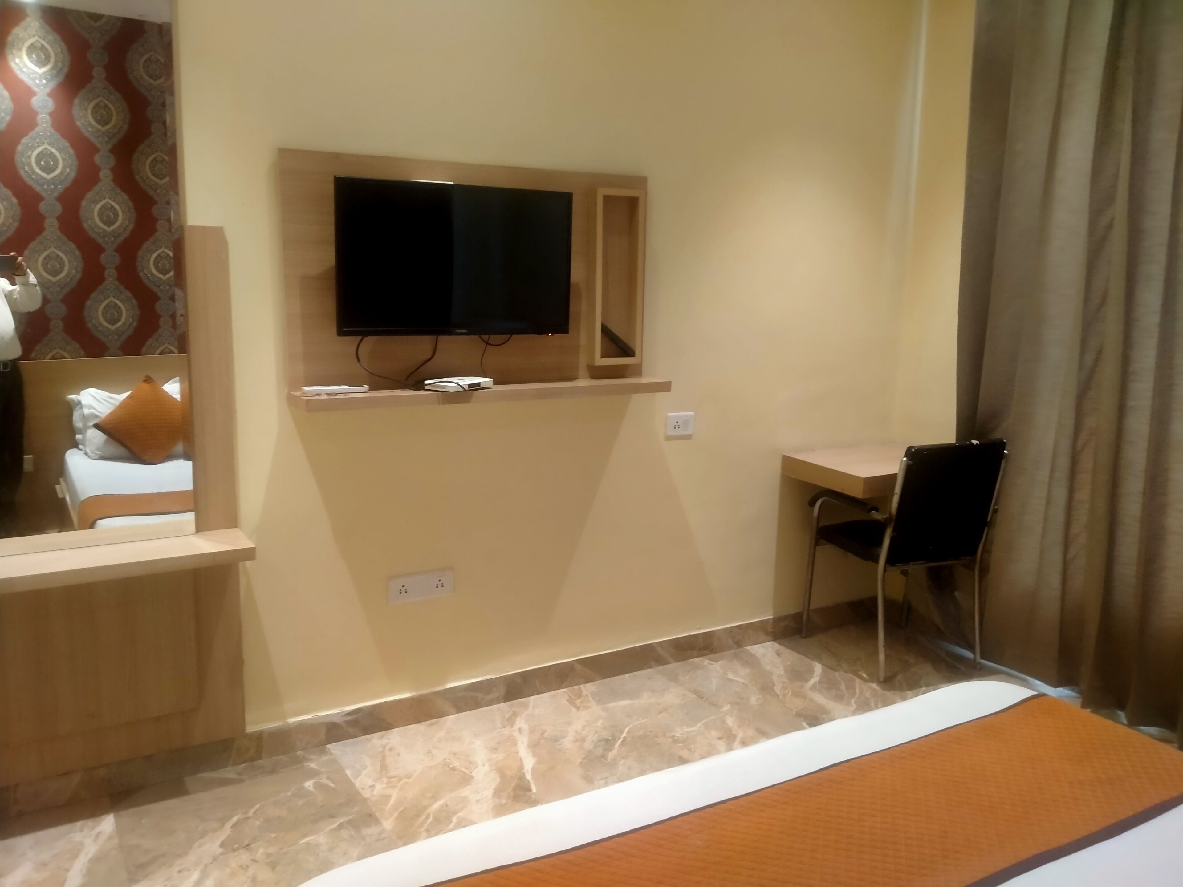 A hotel room with a bed, a desk, a television mounted on the wall, and a mirror.