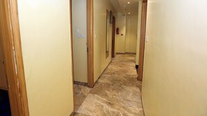 A hotel hallway with marble flooring, wooden doors, and a fire extinguisher on the wall. - HOTEL TRADITION (Amritsar)