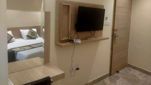 A hotel room with a bed, a television mounted on the wall, a mirror, and a door. - HOTEL TRADITION (Amritsar)