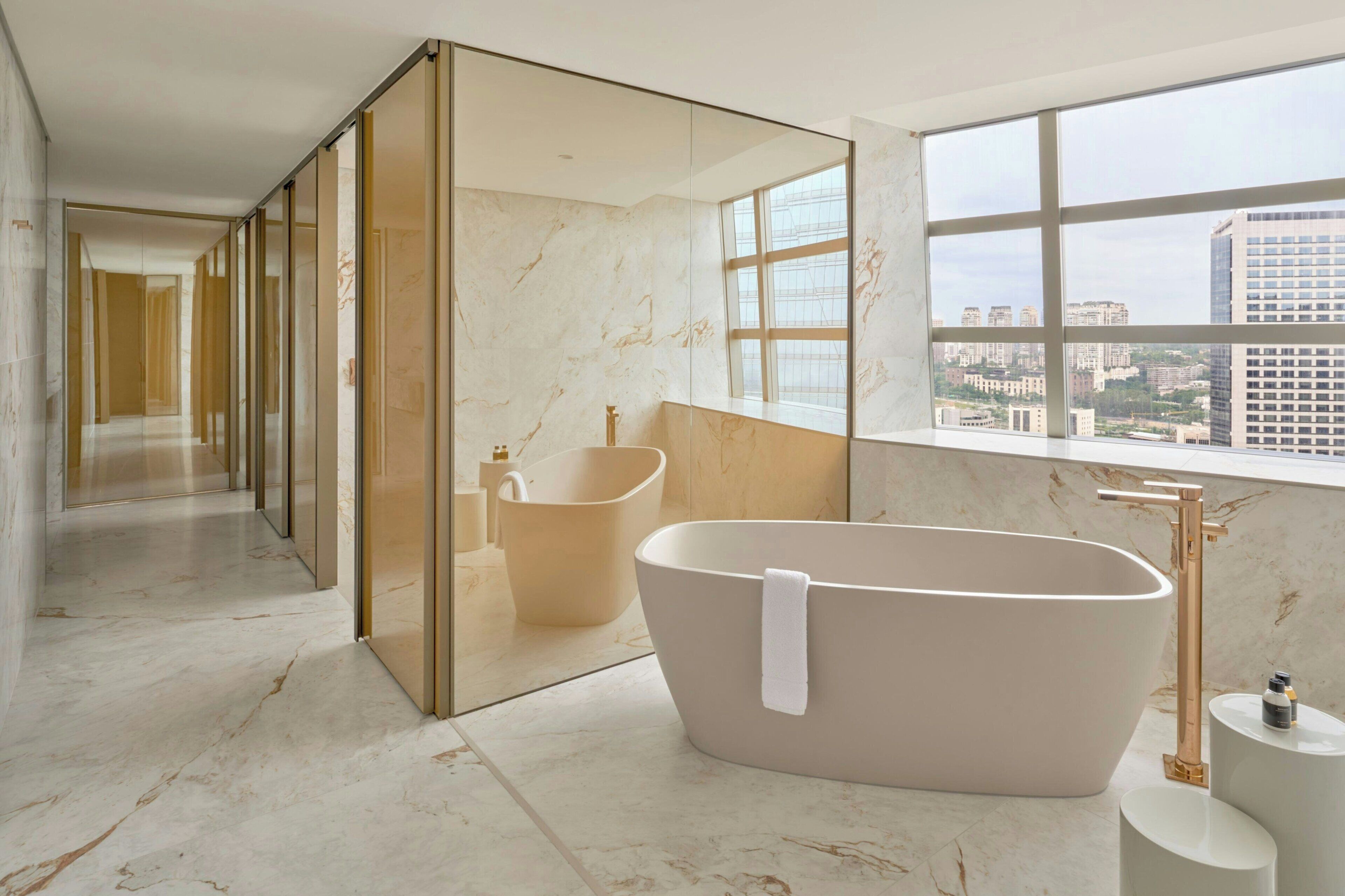 Ein modernes Badezimmer mit einer freistehenden Badewanne, einem großen Spiegel und Stadtblick durch hohe Fenster.