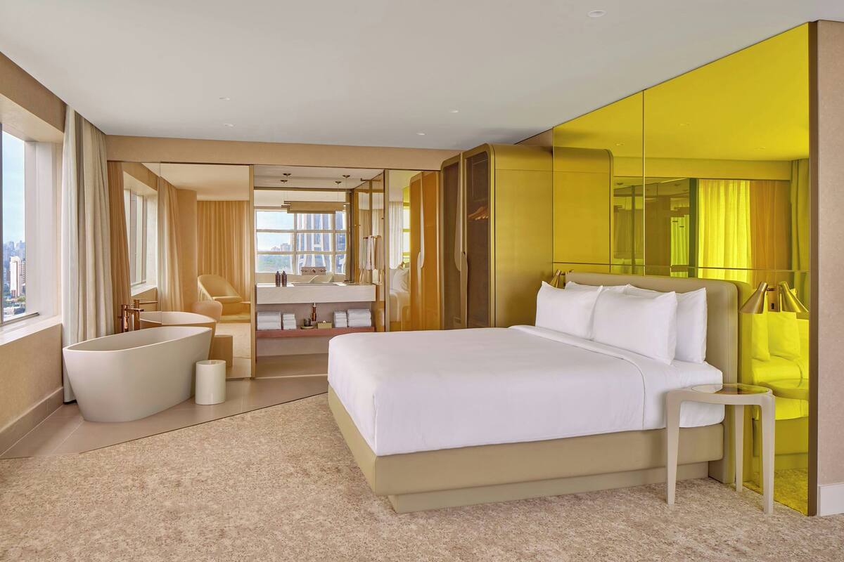 A modern hotel room with a large bed, a bathtub, and a city view.