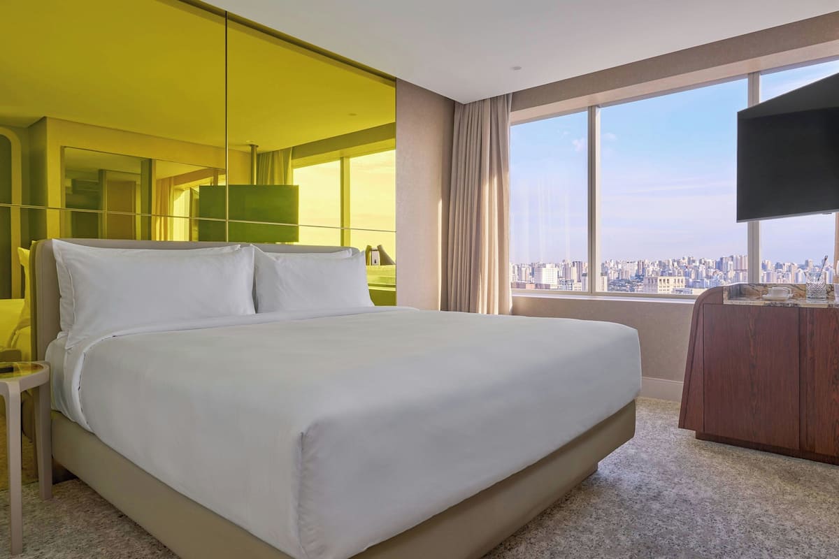 Habitación de hotel con una cama grande, televisión, vista a la ciudad y un espejo.