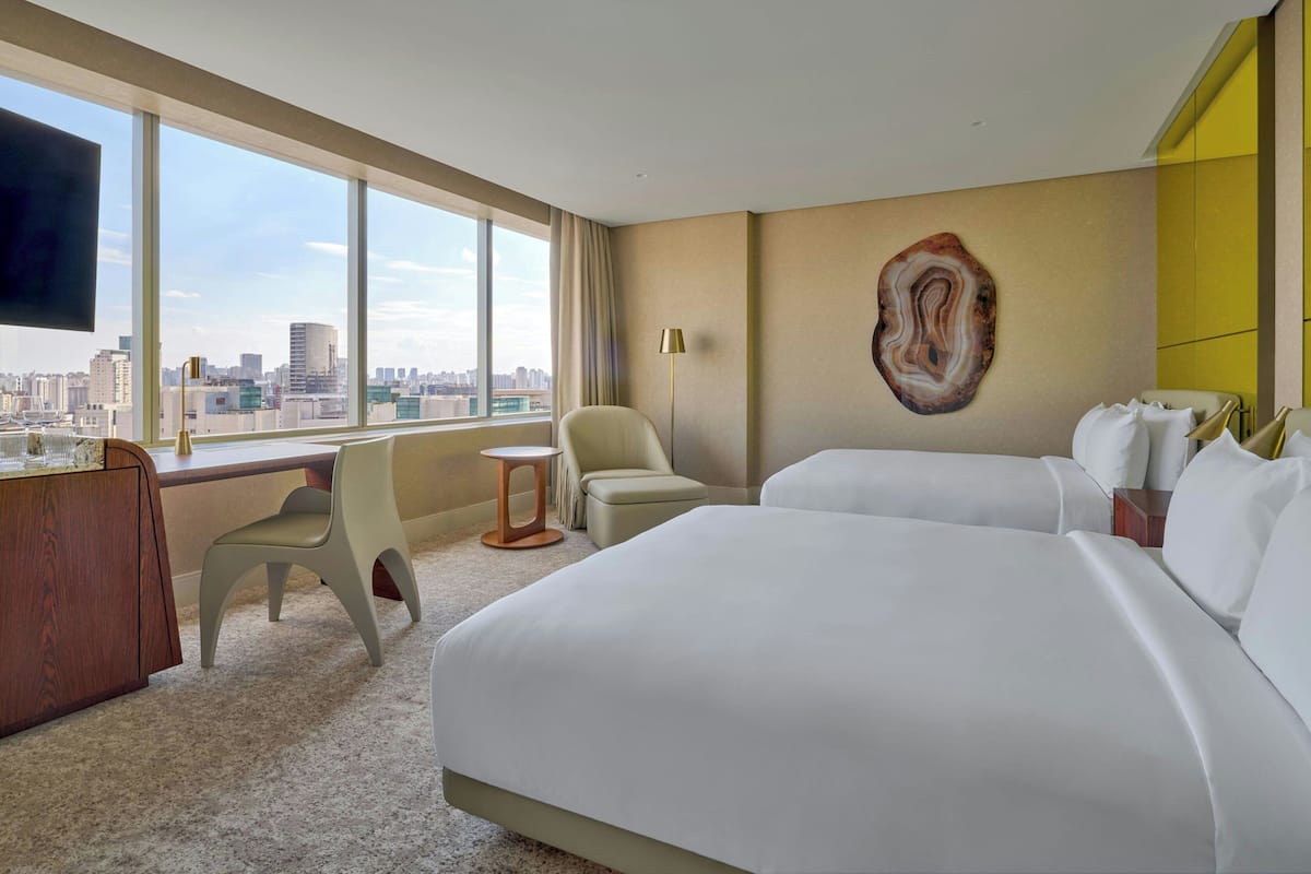 A hotel room with a large bed, a desk, a chair, and a view of the city.