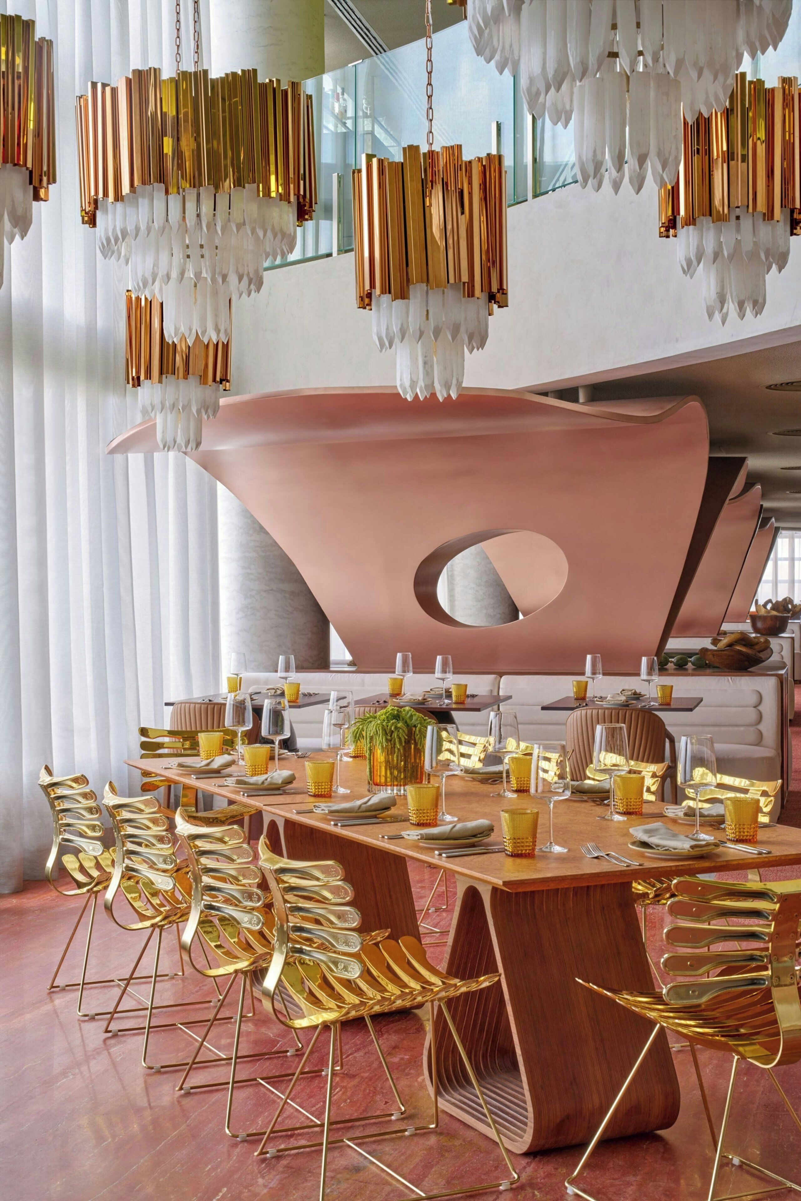 Un comedor con una gran mesa de madera, sillas doradas y candelabros colgantes.