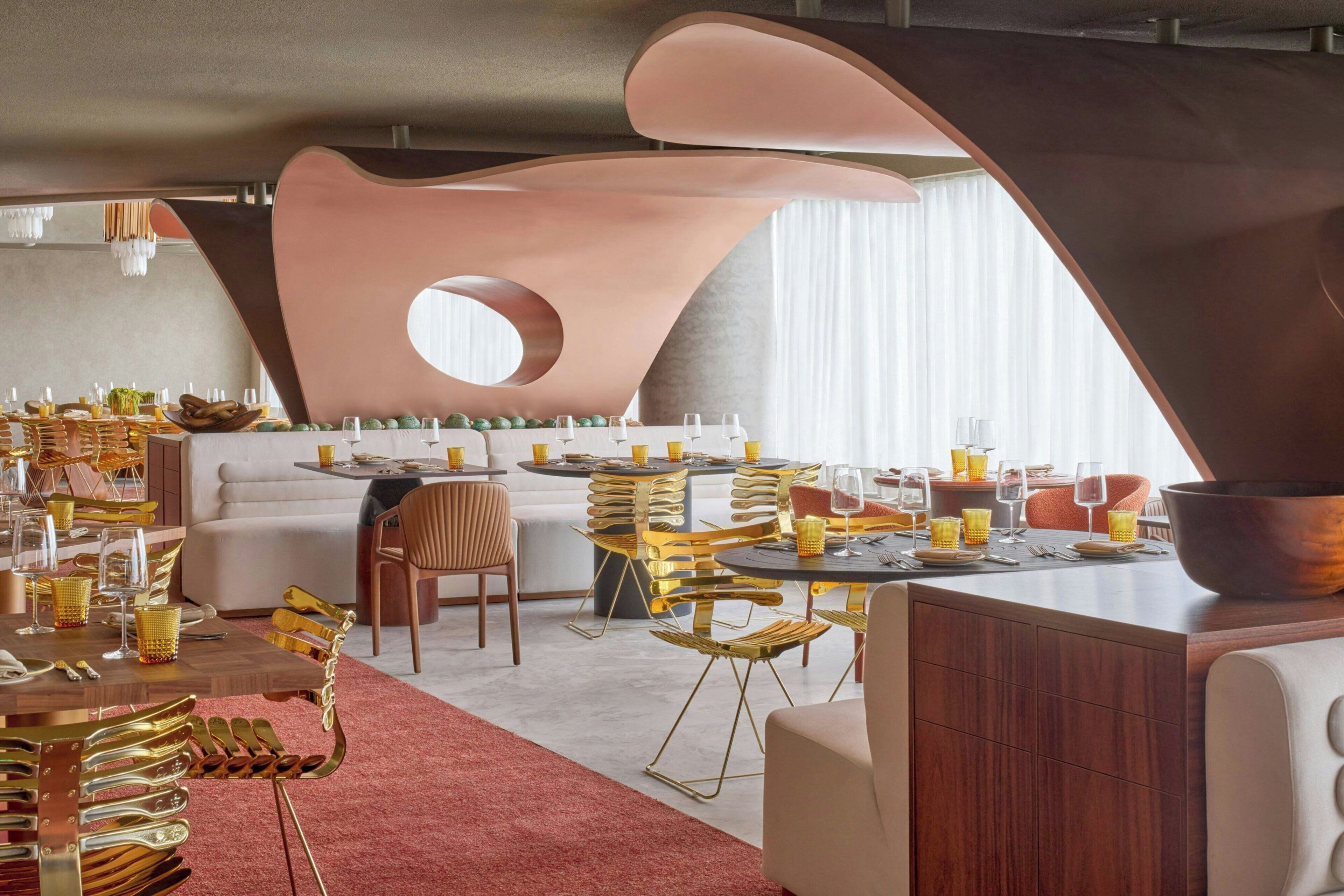A modern dining area with a central round table, surrounded by golden chairs and a sofa.