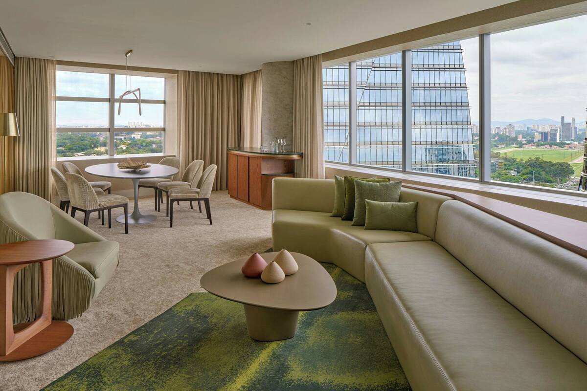 A modern living room with a large window, a round coffee table, a sofa, and a dining area with chairs and a glass table.