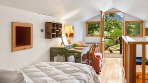 A bedroom with a bed, a desk, and a view of the outdoors.