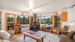 A cozy living room with a fireplace, large windows, and a view of the mountains.