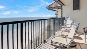 Ein Balkon mit Blick auf Strand und Meer, mit Metallstühlen und einem kleinen Tisch.