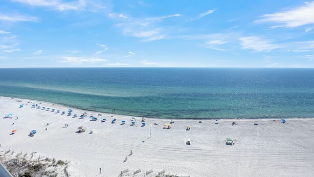 Ein Strand mit Reihen von Sonnenschirmen und Liegestühlen, ein sandiger Uferstreifen und das Meer im Hintergrund.