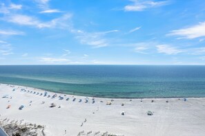 A beach with rows of umbrellas and beach chairs, a sandy shore, and the ocean in the background.