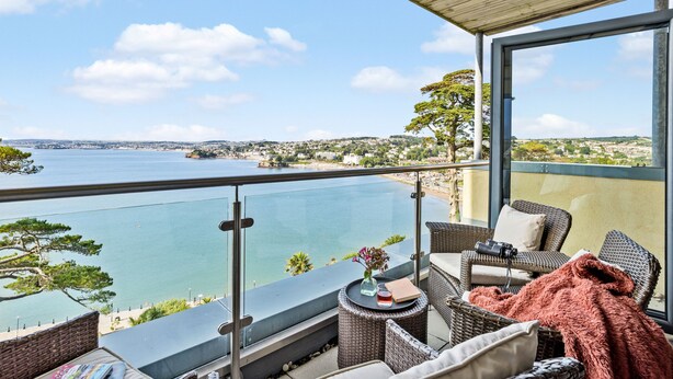 Un balcone con mobili in vimini, vista sul mare e cielo sereno.