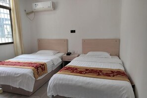 Une chambre d’hôtel avec deux lits simples, une table de chevet avec une lampe, une fenêtre avec des rideaux et un appareil de climatisation fixé au mur.