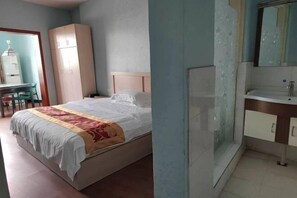 Quarto com cama, guarda-roupa, escrivaninha e banheiro com pia e espelho.