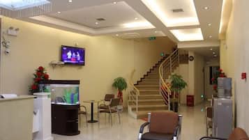 A hotel lobby with a reception desk, a fish tank, a staircase, and a television.