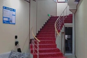 Un escalier recouvert d’une moquette rouge, avec des rampes blanches et une porte en bas.
