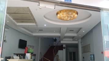 A hotel reception area with a staircase, a reception desk, and a large chandelier.
