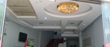 Zona de recepción de un hotel con escalera, mostrador de recepción y una gran araña.