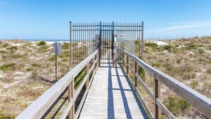 Une promenade en bois menant à une plage, avec une barrière métallique et un panneau.