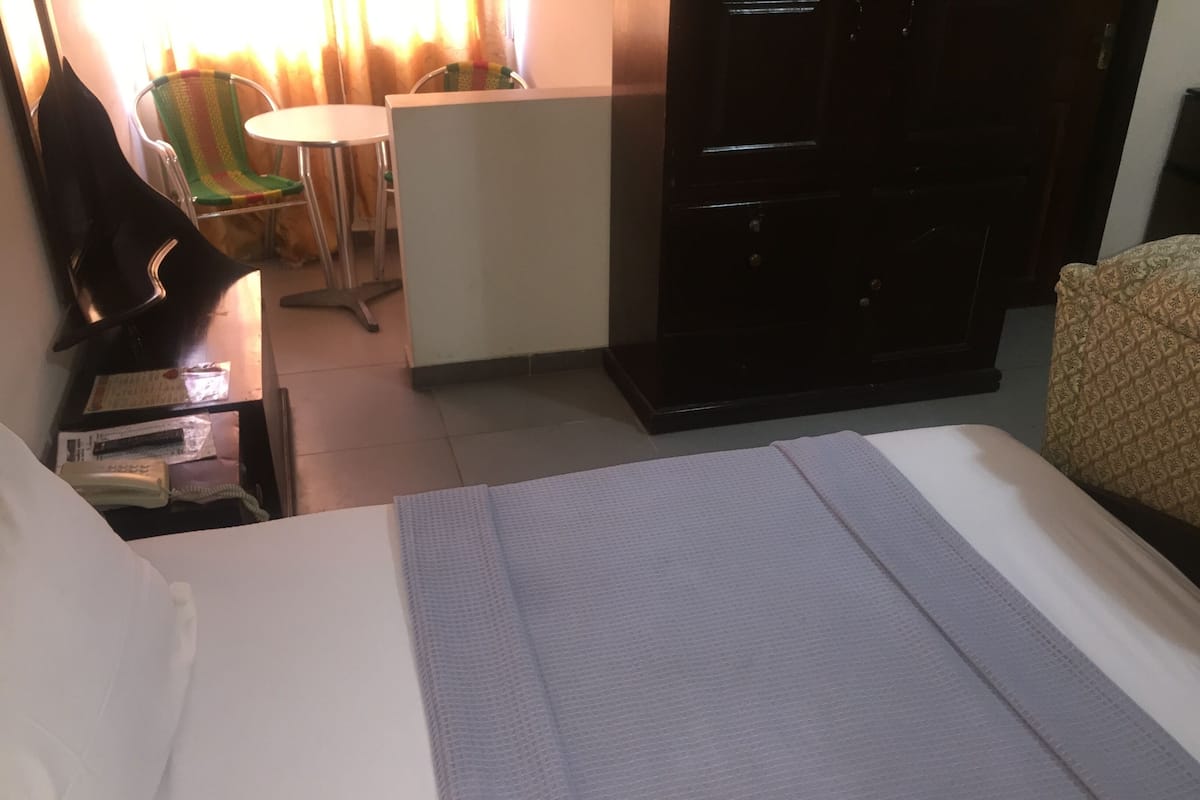 A hotel room with a bed, a desk with a telephone, a chair, and a small table.