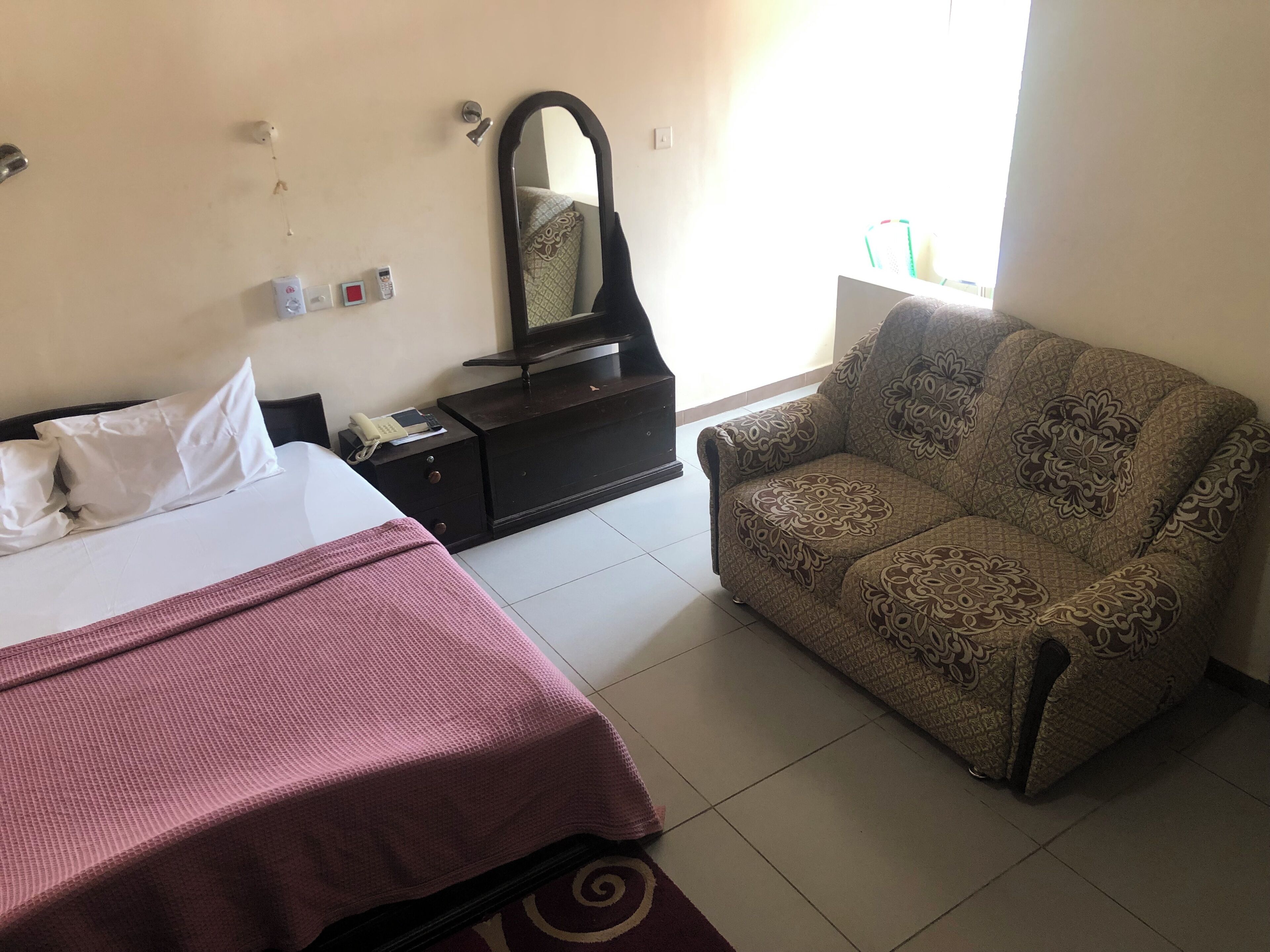 A hotel room with a bed, a sofa, a dresser, a mirror, and a window.
