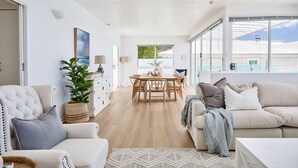 A spacious living area with a dining table, sofas, and a large window offering a view of the outdoors. - Waterfront Oasis with Infinity Pool and Stunning River Views (Taroona)