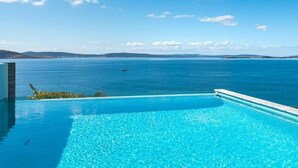 A clear blue infinity pool with a view of the ocean and distant hills. - Waterfront Oasis with Infinity Pool and Stunning River Views (Taroona)