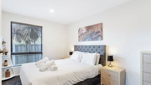 Une chambre d’hôtel moderne avec un grand lit, une table de chevet avec une lampe, un tableau au mur et une fenêtre avec des stores.