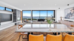 Un salon moderne doté d’une table à manger en verre, de sièges confortables, d’une cheminée et d’une grande fenêtre offrant une vue sur la mer.