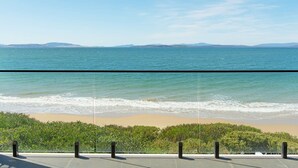 Une vue sur l’océan depuis un balcon, avec un ciel dégagé et des montagnes à l’horizon.
