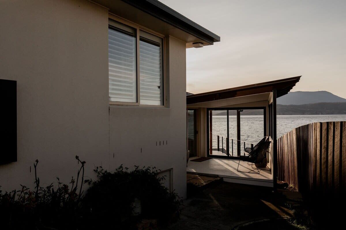 A modern house with a large glass door leading to a deck overlooking a body of water.
