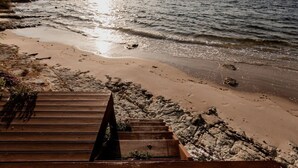 Un escalier en bois descend vers une plage de sable où les vagues se brisent.