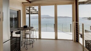 Un balcon avec une table et des chaises, donnant sur une étendue d’eau et sur une terre lointaine.