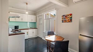 Una cocina compacta con armarios blancos, una mesa de comedor y un refrigerador.