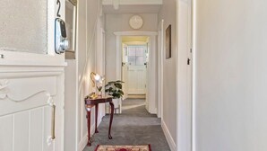 A hallway with a white door, a clock, a small table with a lamp, and a red rug.