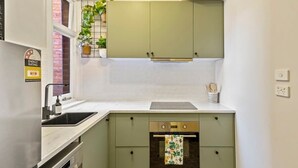 A compact kitchen with a built-in oven, a sink, and a window with a plant.