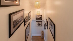 Un pasillo con fotografías enmarcadas en las paredes, una escalera de madera y una lámpara colgante.