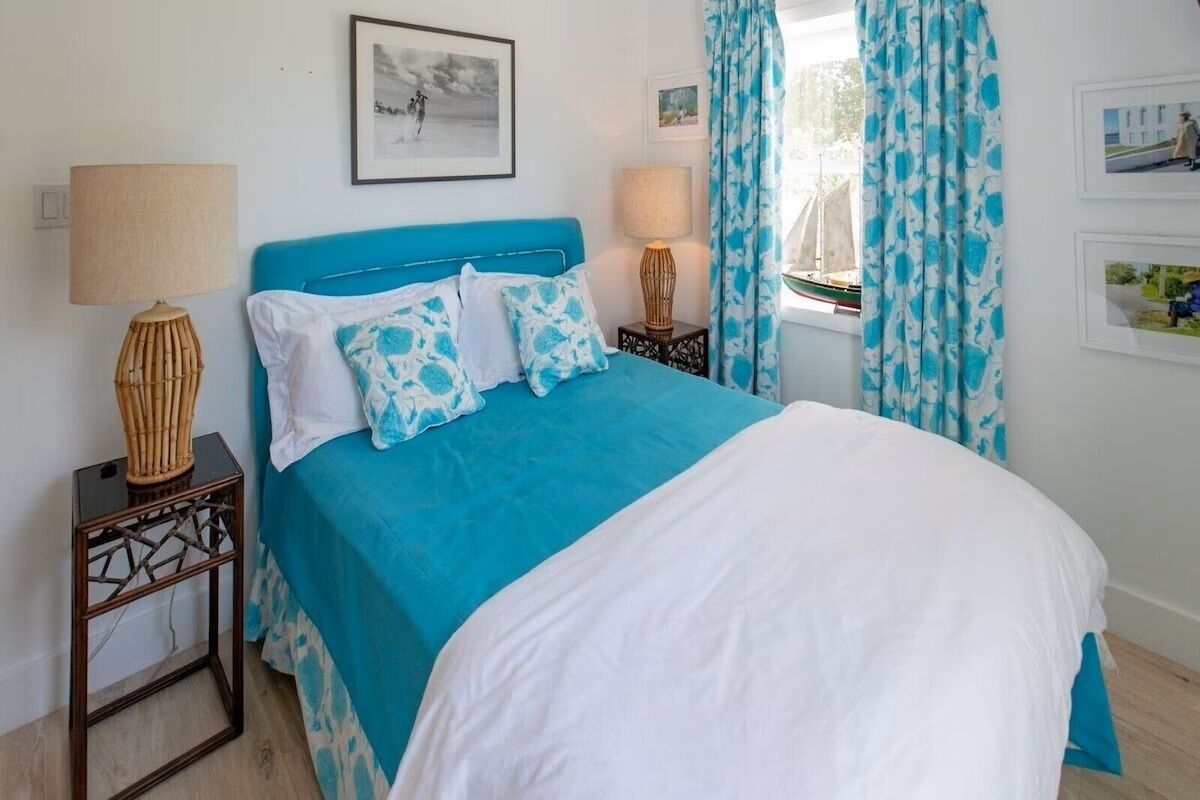 A bedroom with a blue bedspread, white pillows, a wooden nightstand, and a lamp.