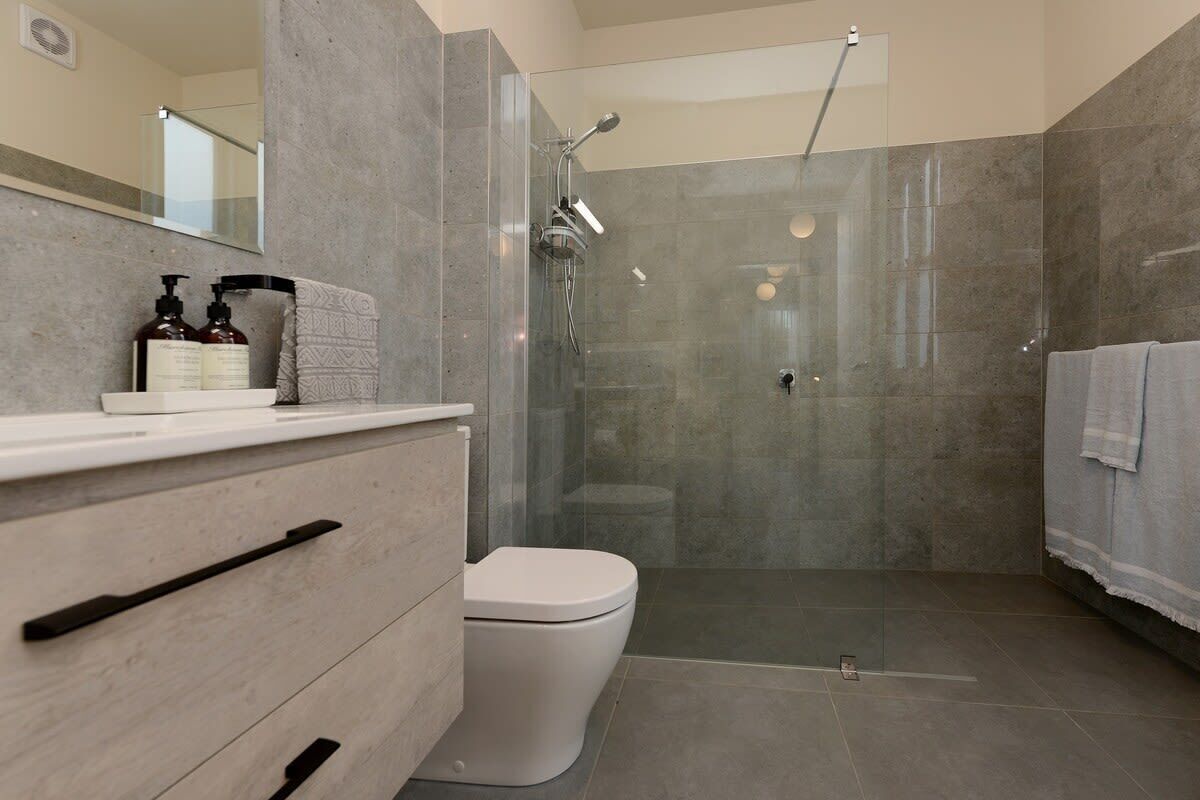 Une salle de bain moderne avec une douche à parois de verre, des toilettes blanches et un meuble-lavabo doté d’un miroir et d’articles de toilette.