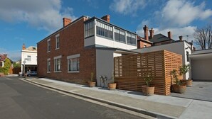 Une maison moderne à deux étages, avec une façade en briques, de grandes fenêtres et une clôture en bois.