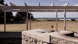 An outdoor seating area with a stone wall and a white pergola overlooking a beach. - Waterfront Boltons Beach Cottages - room for 8 (Triabunna)