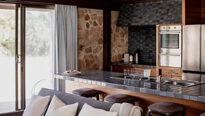 A modern kitchen with a stone wall backsplash, a built-in oven, and a bar area with stools. - Waterfront Boltons Beach Cottages - room for 8 (Triabunna)