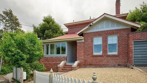 Ein zweistöckiges Backsteinhäuschen mit Veranda, Garage und weißem Zierzaun.