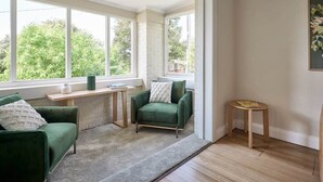 Ein Zimmer mit großem Fenster, einem grünen Sofa, einem kleinen Tisch und Holzboden.