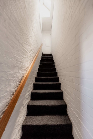 A staircase with a handrail leads upwards, flanked by textured walls.