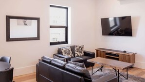 A modern living room with a leather sofa, a coffee table, and a flat-screen TV mounted on the wall. - 3 Bedroom, Spacious Inner-City Pad (Hobart)