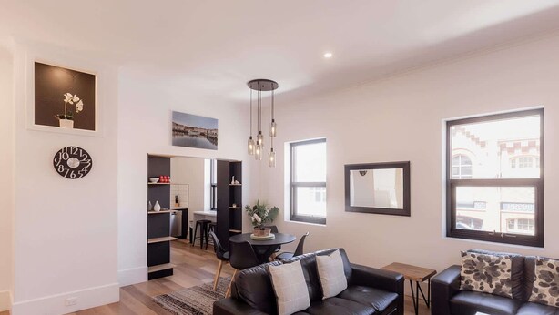 A modern living room with a black leather sofa, a dining area with a small table and chairs, and a kitchen in the background. - 3 Bedroom, Spacious Inner-City Pad (Hobart)